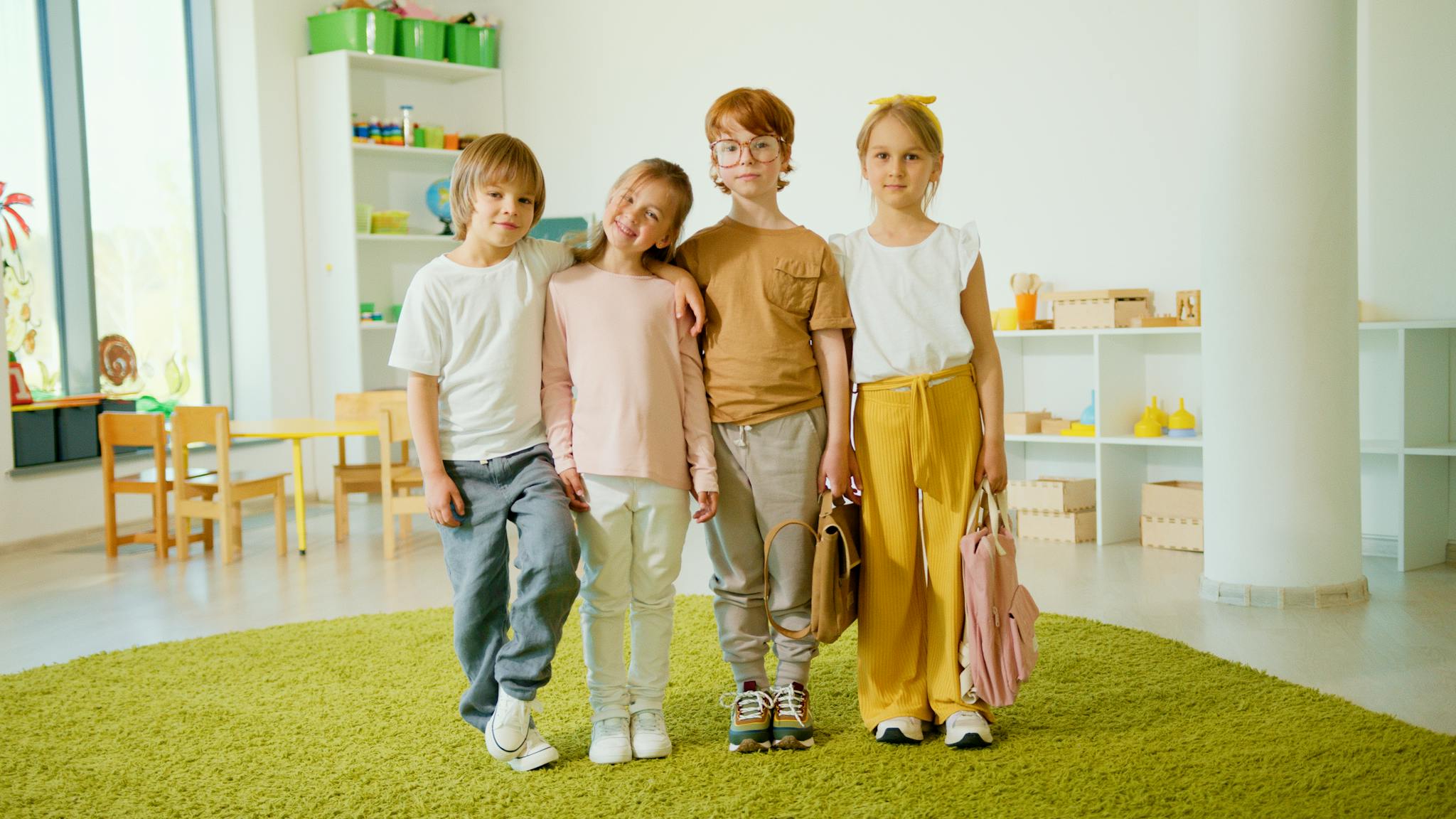 A group of four smiling children standing together in a bright classroom.