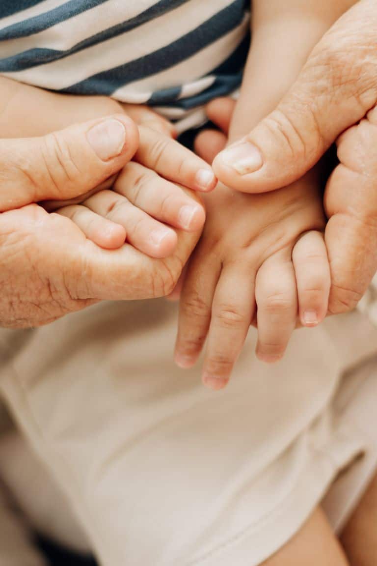 Close-up of elderly and baby hands touching, symbolizing connection across generations.